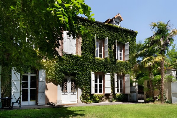 A two-story building with a garden in front. - Room "Room 5" with Shared Terrace, Shared Garden and Wi-Fi (Vic-en-Bigorre)