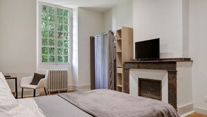 Une chambre à coucher comprenant un lit, une chaise, une télévision, une cheminée et une fenêtre donnant sur la forêt.