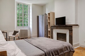 A bedroom with a bed, a chair, a television, a fireplace, and a window with a view of trees. - Room "Room 5" with Shared Terrace, Shared Garden and Wi-Fi (Vic-en-Bigorre)