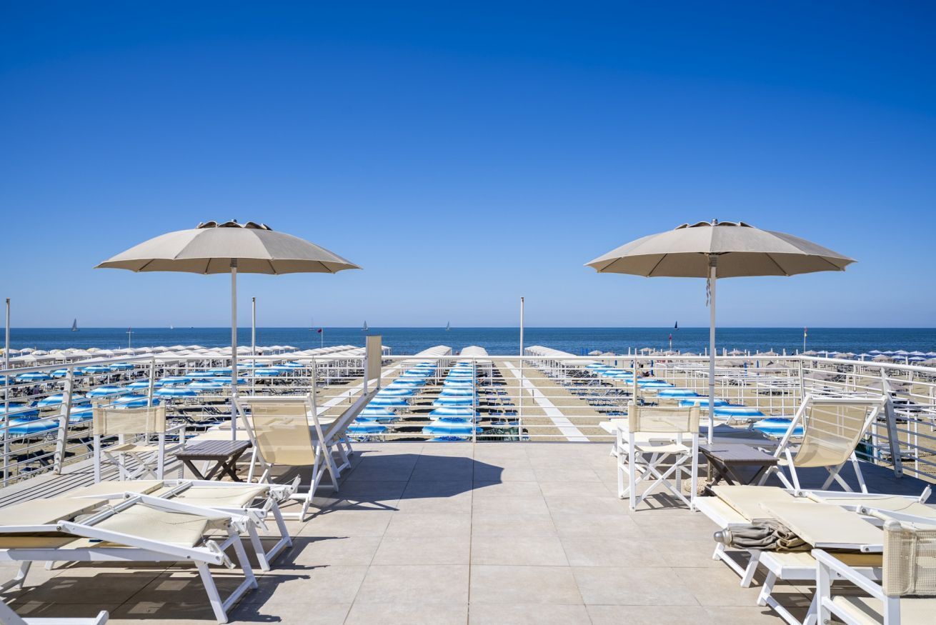 Eine Strandterrasse mit Liegestühlen und Sonnenschirmen, mit Blick aufs Meer.