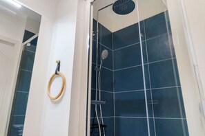 Une douche Ă©quipĂ©e dâun pommeau de douche Ă main, dâun pommeau de douche circulaire fixĂ© au mur et dâun anneau en bois sur le mur.