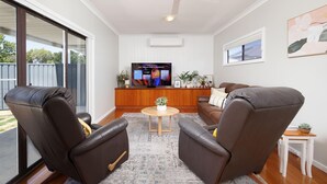 Una sala de estar con un televisor de pantalla plana grande, dos sillones de cuero, una mesa de centro y una mesita auxiliar.