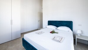 Quarto moderno com cama grande, roupa de cama branca, cabeceira verde-água e mesa de cabeceira com abajur.