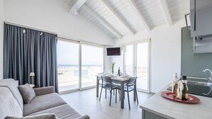 Uma sala de estar moderna com sofá cinzento, área de jantar com mesa e cadeiras, cozinha com pia e TV de tela plana na parede.