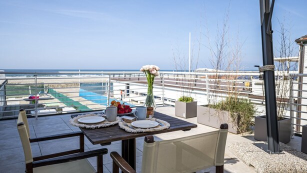 Espaço de refeições com mesa posta para dois, com vista para uma piscina e o oceano.
