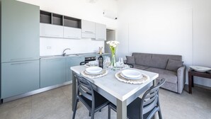 Uma cozinha moderna com armários azul-claros, uma mesa de jantar posta com pratos e copos, e um sofá cinza na sala de estar.