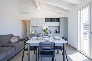 Eine moderne Küche mit weißen Schränken, einem Esstisch für sechs Personen und einem grauen Sofa mit Zierkissen.