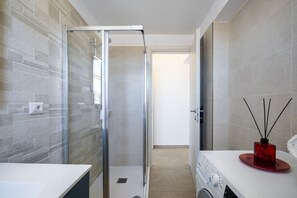 Ein modernes Badezimmer mit Duschkabine aus Glas, einem weißen Waschbecken und einem roten Diffusor auf der Ablagefläche.