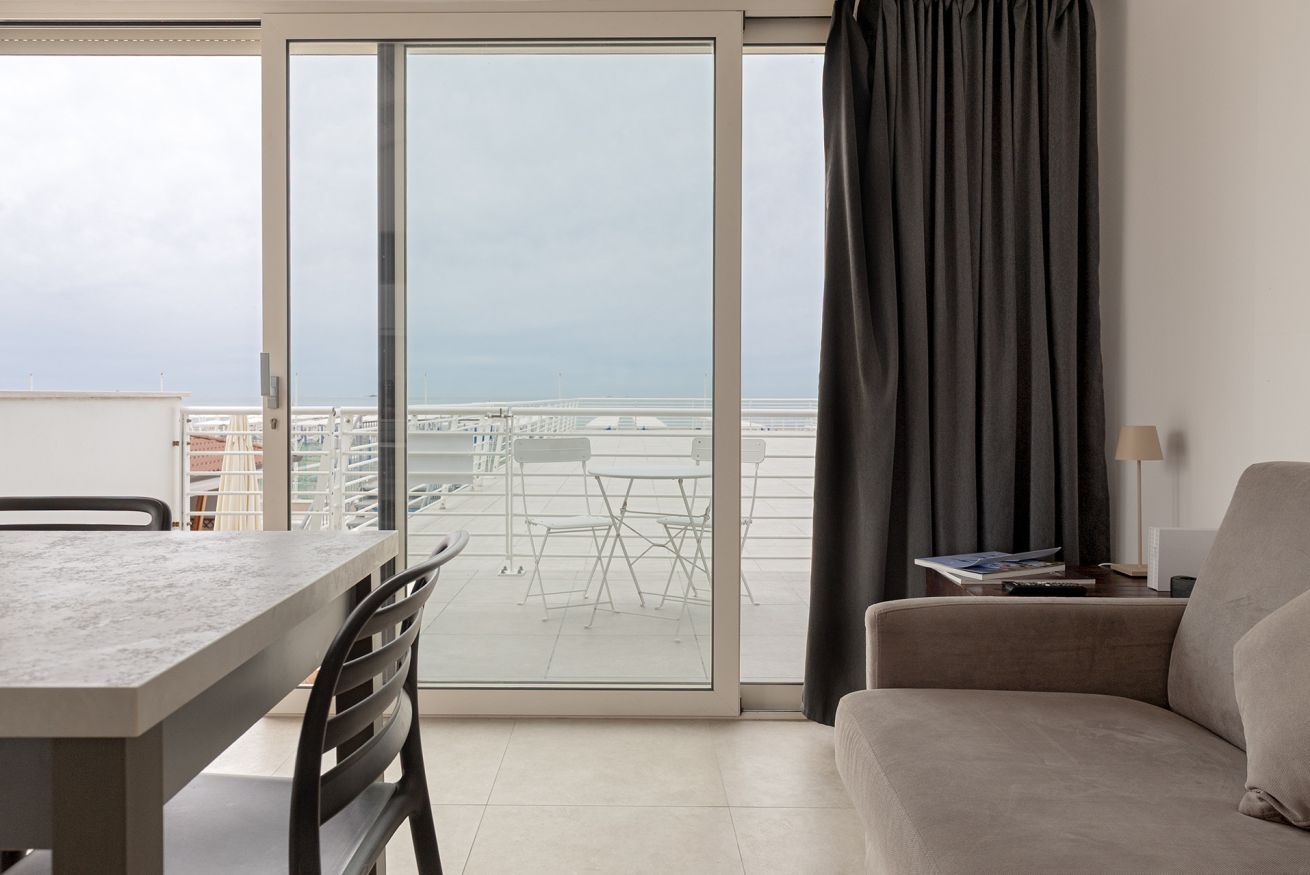 A modern living room with a dining area, a sofa, a table, and a view of the sea through large glass doors.