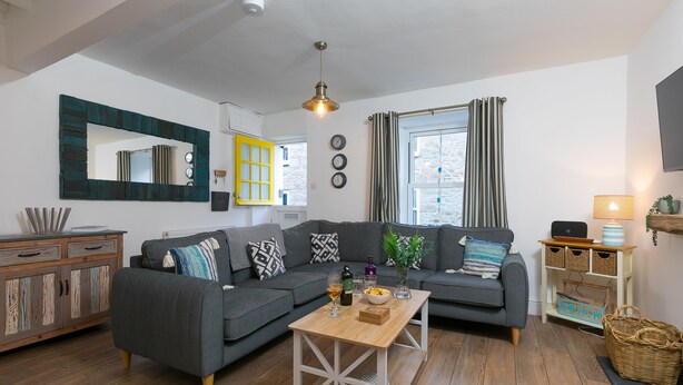 A modern living room with a grey sectional sofa, a wooden coffee table, and a large mirror with a unique frame. - Dan’s Den, St Ives– Sleeps 4 – Dog Friendly – Wood Burner (St Ives)