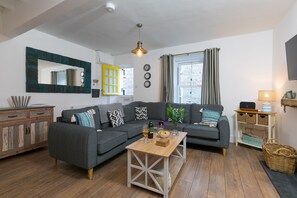 A modern living room with a grey sectional sofa, a wooden coffee table, and a large mirror with a unique frame. - Dan’s Den, St Ives– Sleeps 4 – Dog Friendly – Wood Burner (St Ives)