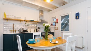 A modern kitchen with white cabinets, a wooden table, and a blue vase with flowers. - Dan’s Den, St Ives– Sleeps 4 – Dog Friendly – Wood Burner (St Ives)