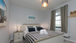 A neatly arranged bedroom with a bed, bedside tables, a lamp, a framed picture, and a window with curtains. - Dan’s Den, St Ives– Sleeps 4 – Dog Friendly – Wood Burner (St Ives)