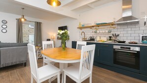 A modern kitchen with white cabinets, a wooden dining table, and a built-in oven. - Dan’s Den, St Ives– Sleeps 4 – Dog Friendly – Wood Burner (St Ives)