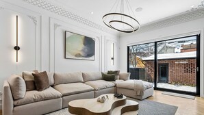 Ein modernes Wohnzimmer mit einem Ecksofa, einem einzigartigen Holztisch und einem großen Fenster mit Blick auf ein Backsteinhaus.