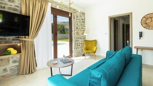 Una sala de estar con una pared de piedra, un sofá verde azulado y un sillón amarillo, además de un televisor.