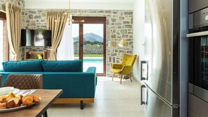 Una sala moderna con sofá, mesa de comedor con cruasanes, televisor y cocina con un refrigerador grande.