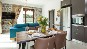Una sala de estar moderna con un sofá azul, una mesa de comedor para dos personas y una cocina con armarios oscuros y un refrigerador de acero inoxidable.