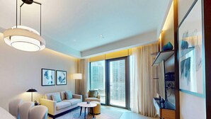Quarto de hotel moderno com sofá, poltronas, mesa de centro e TV sobre suporte.
