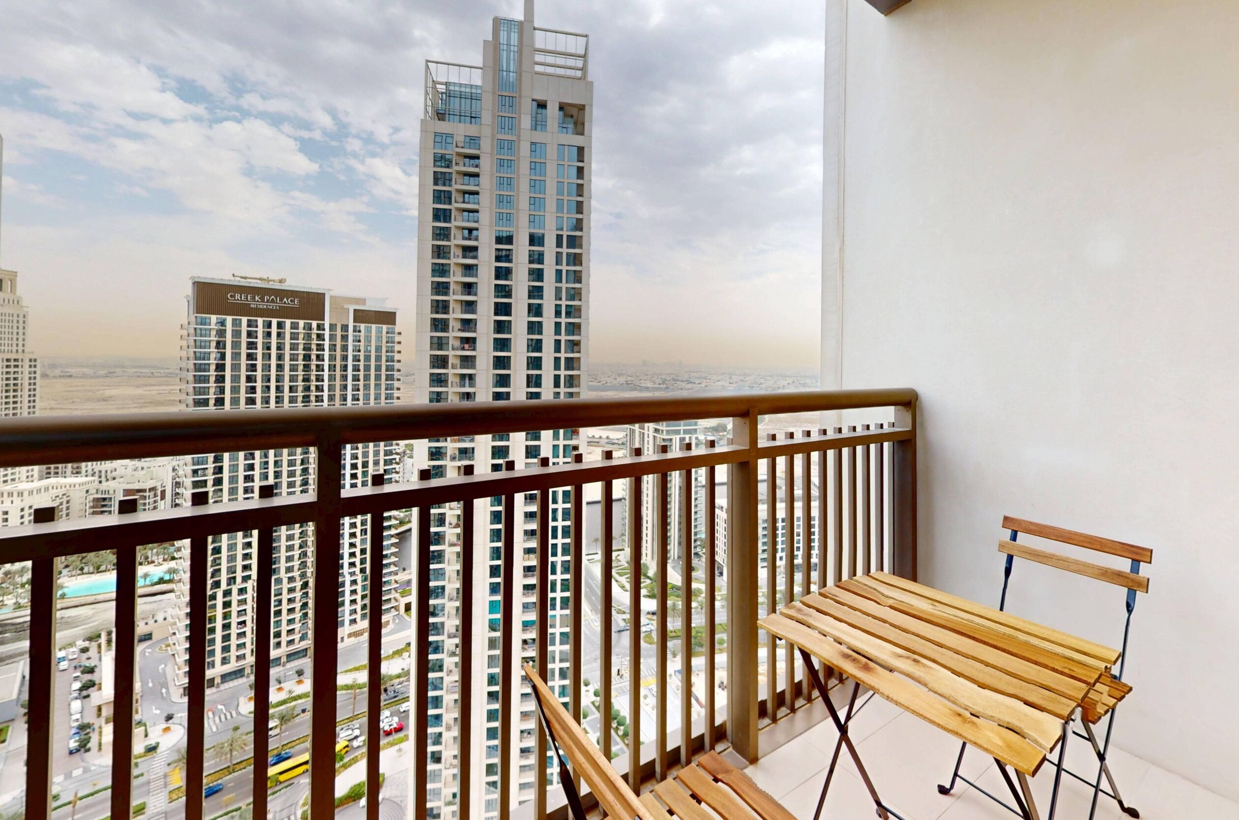 Ein Balkon mit einer hölzernen Sitzbank und Blick auf hohe Gebäude, darunter das mit 'Creek Palace' beschriftete.