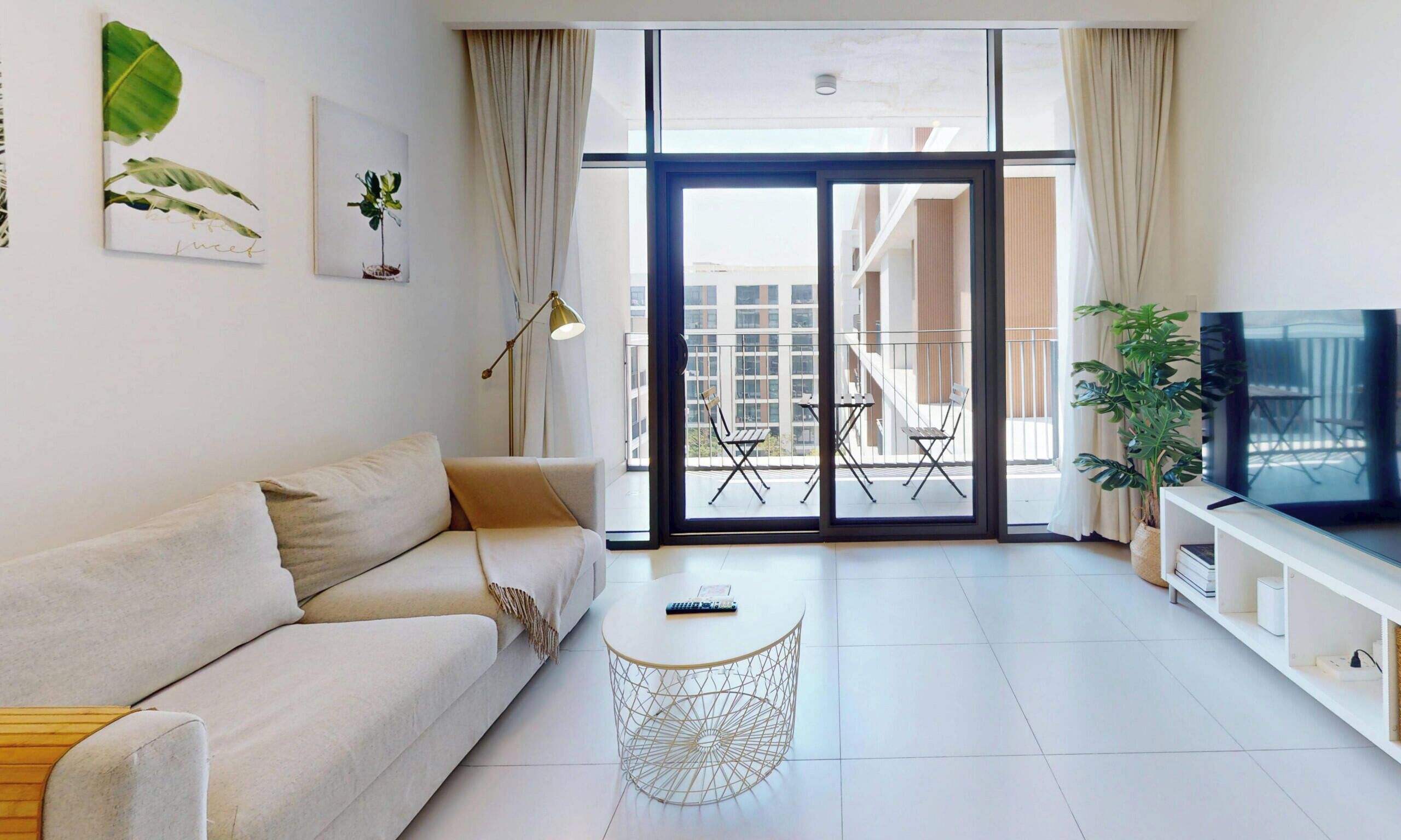 A modern living room with a sofa, a coffee table, a TV, and a balcony with outdoor furniture.