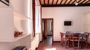 Zona pranzo con tavolo e sedie in legno, televisore montato a parete e finestra con tende.