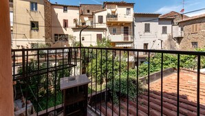 Un balcone con vista su edifici dalle tegole rosse, ringhiera in metallo e piante in vaso.