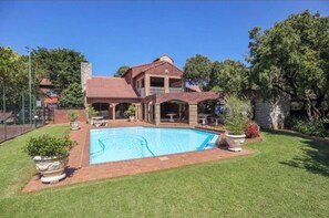 Une maison avec une piscine, entourée d’une pelouse bien entretenue et d’arbres.