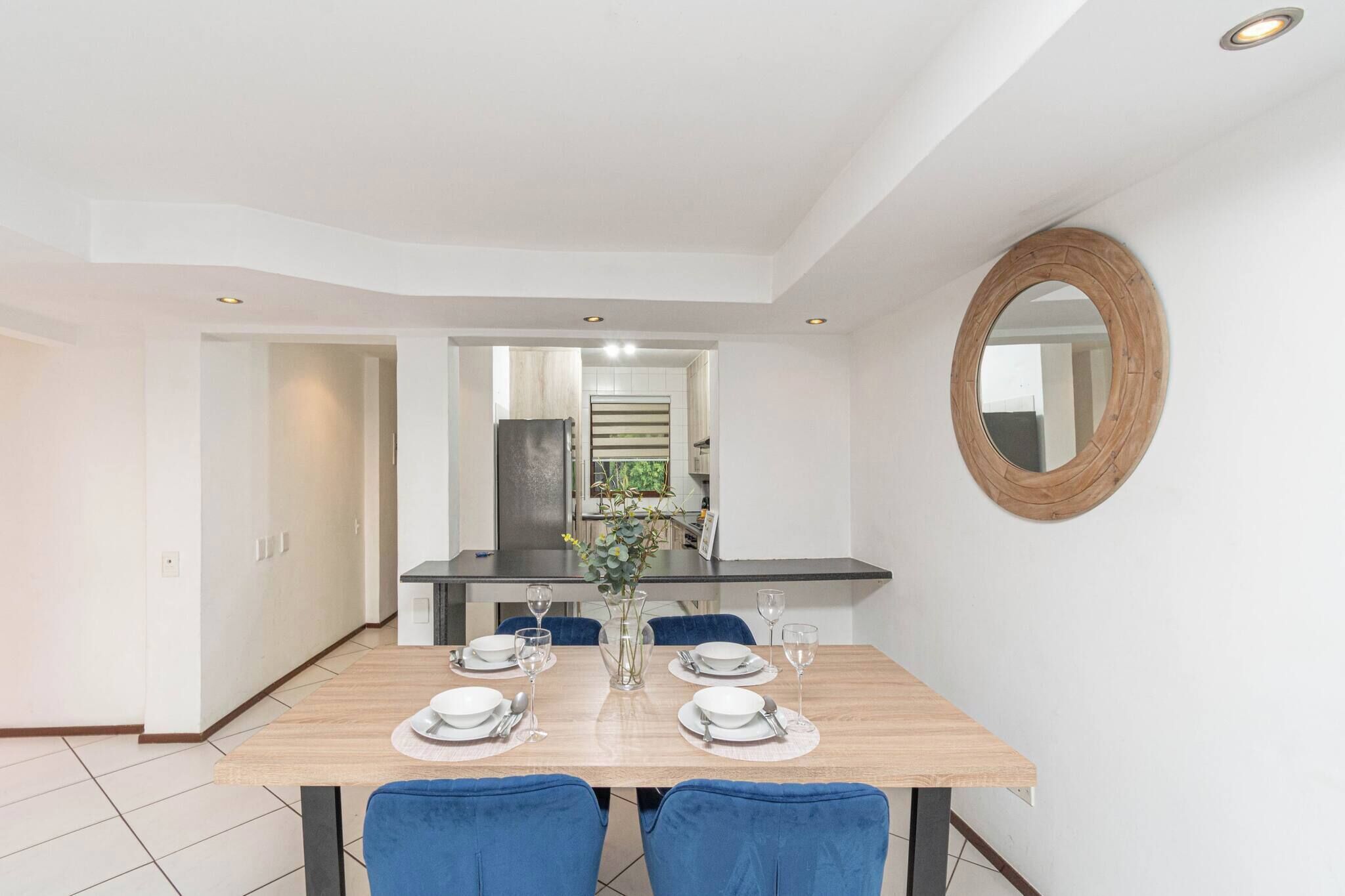 A modern dining area with a wooden table set for four, blue chairs, and a mirror on the wall.