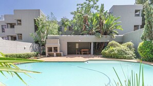 Um edifício moderno com piscina, rodeado por vegetação e um céu claro.
