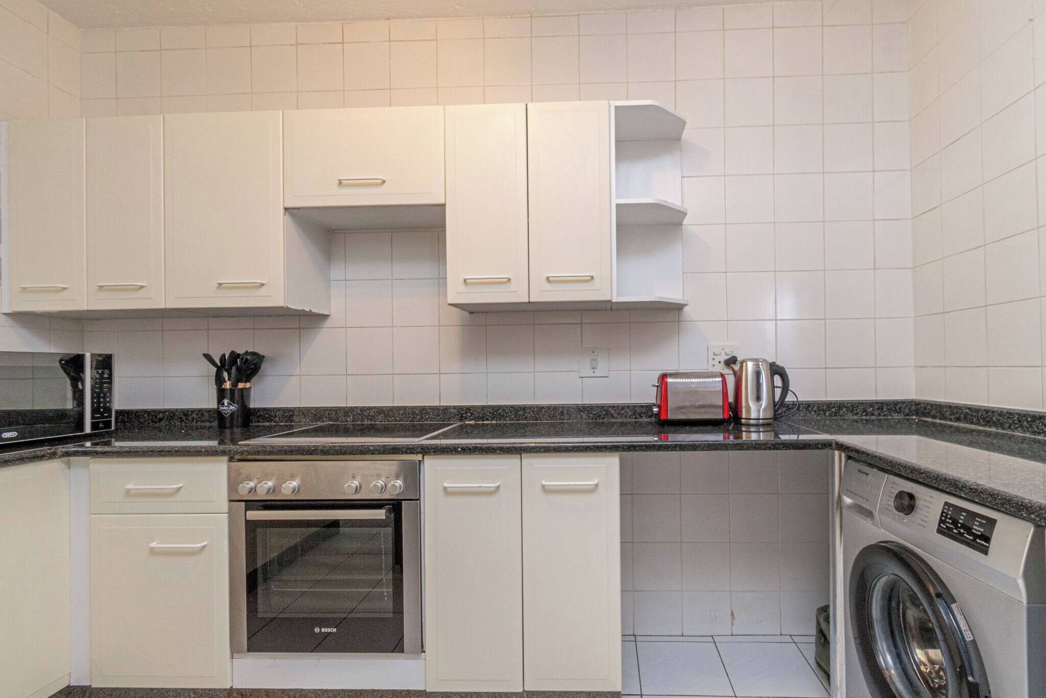 Una cocina compacta con armarios blancos, horno Bosch, lavadora y microondas.