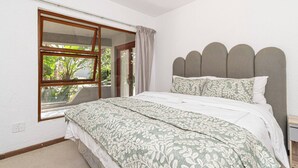 Quarto com uma janela grande, cama com roupa de cama estampada e cabeceira com design recortado.