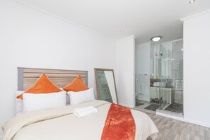 Et moderne hotelværelse med en stor seng, en glasbrusekabine og en hvid væg.