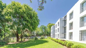 Un edificio moderno con fachada blanca, varios balcones y un jardín cuidado con árboles y arbustos.