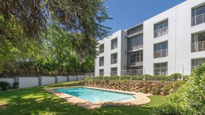 Un edificio moderno con una piscina rodeada por un césped cuidado y árboles.