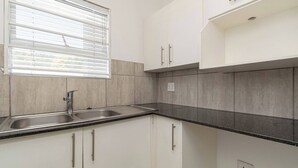 Una cocina con armarios blancos, un lavamanos doble y un ventanal con persianas.
