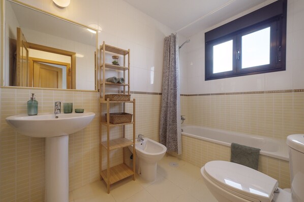 A bathroom with a sink, bidet, toilet, and a window above the bathtub.