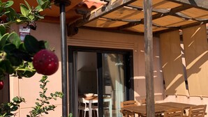 A patio with a wooden table and chairs, a pergola, and a view of the interior through a glass door.
