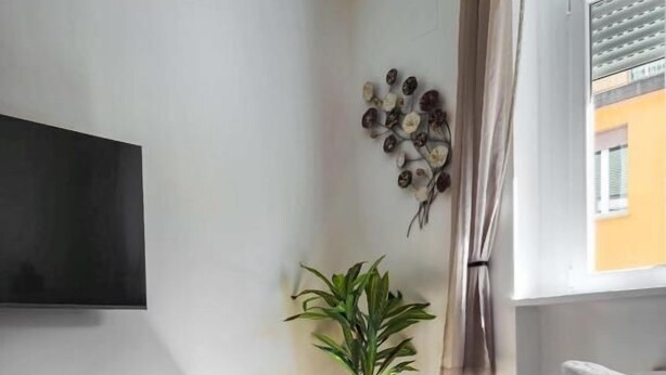 A neatly made bed with a beige textured blanket, a stack of folded towels, a potted plant, and a wall-mounted TV. - Marsala Suites (Bologna)