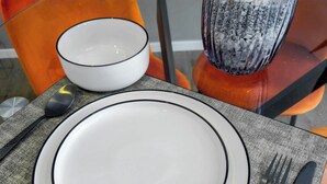 A table set with a white plate, black rimmed bowl, black spoon, black fork, and knife on a textured placemat. - Marsala Suites (Bologna)