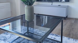A modern living room with a glass coffee table, a potted plant, a flat-screen TV, and a white entertainment unit. - Marsala Suites (Bologna)
