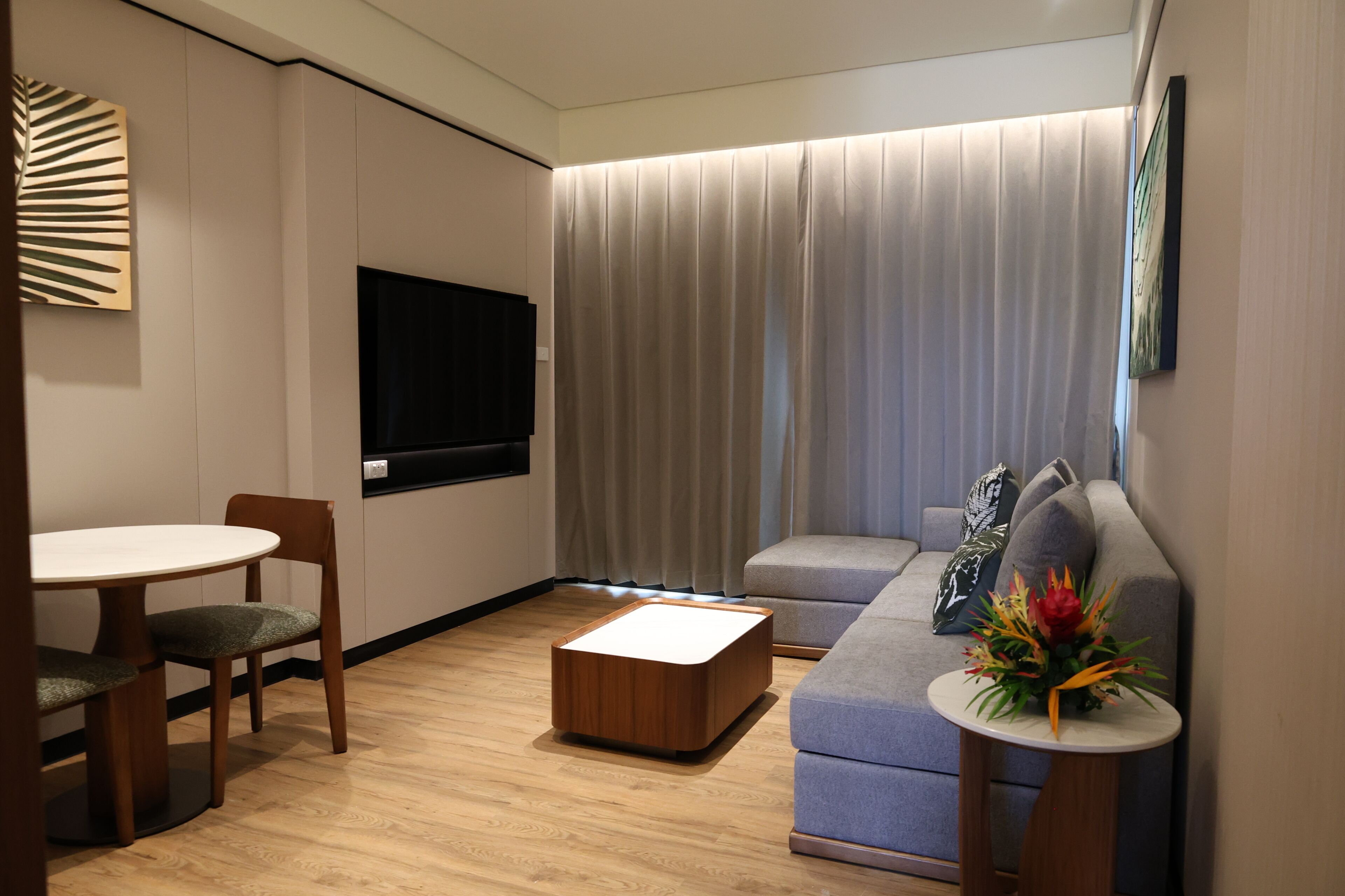 Een moderne woonkamer met een flatscreen televisie, een bank, een salontafel en een eethoek met stoelen.