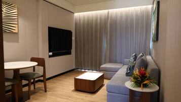 Een moderne woonkamer met een flatscreen televisie, een bank, een salontafel en een eethoek met stoelen.