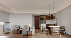 Un salon moderne avec un canapé, une table basse et un coin repas avec des chaises. On aperçoit au fond une cuisine avec des meubles en bois et un réfrigérateur.