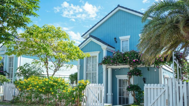 A two-story house with a blue exterior, white trim, and a white picket fence.