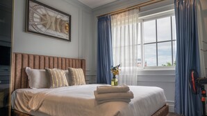 A neatly made bed with pillows, a bedside table with a vase of flowers, and a window with curtains.