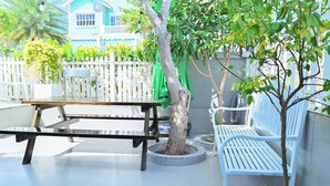 A patio area with a wooden bench, a small tree, and a white fence.