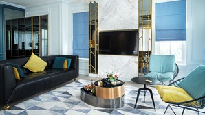 A modern living room with a black sofa, a round coffee table, a blue armchair, and a TV mounted on a marble wall.