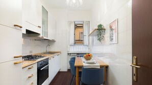 A compact kitchen with white cabinets, a wooden countertop, a gas stove, and a dining area with a table and chairs. - Large Apartment Sesto Rondò M1 - Duomo 20 min (Sesto San Giovanni)