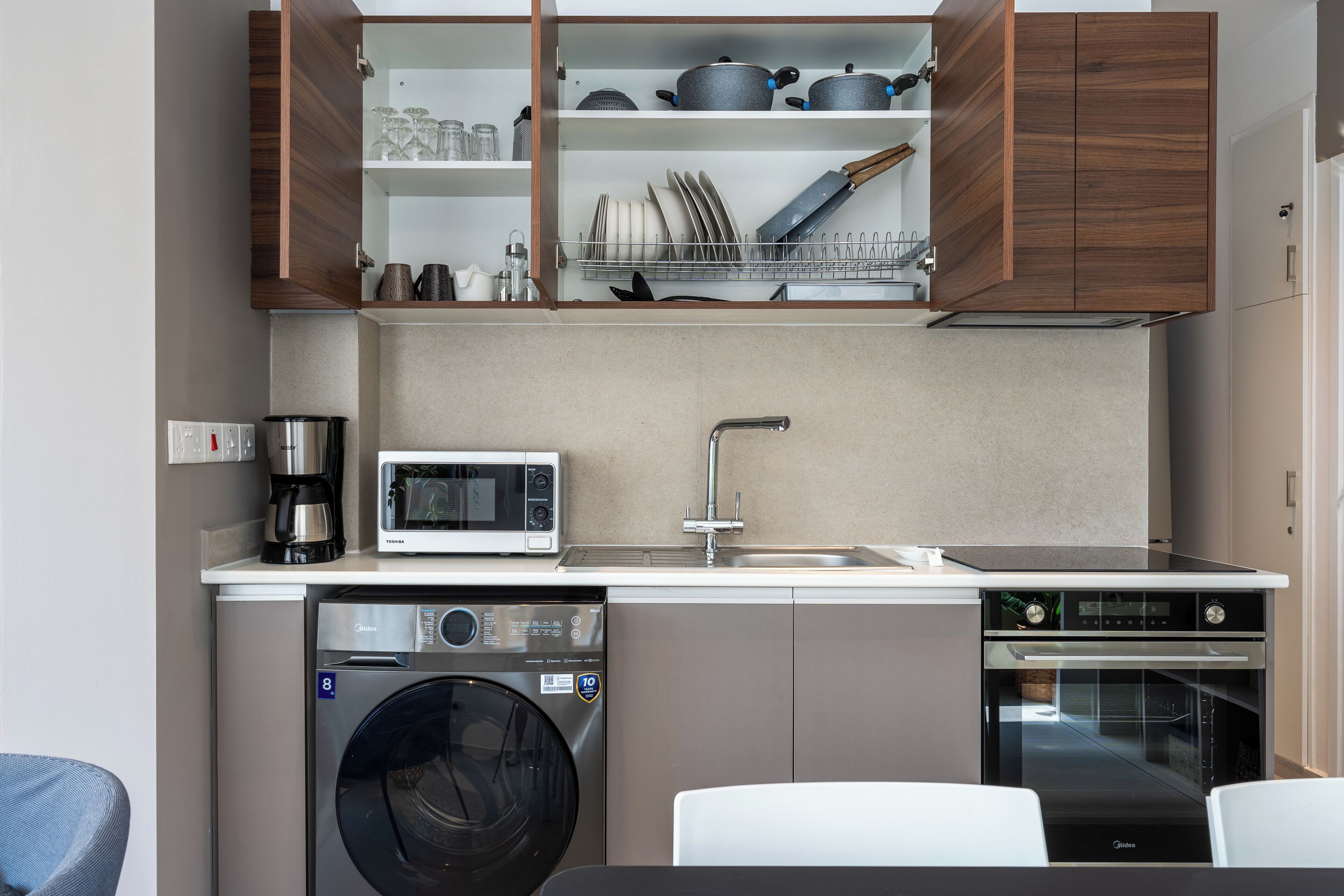 Une cuisine compacte équipée d’un lave-linge, d’un lave-vaisselle, d’un four à micro-ondes et d’un four traditionnel.
